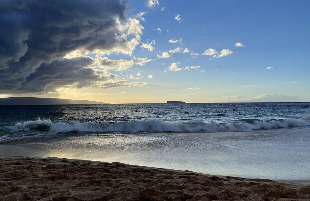 Dark sand shoreline at Oneloa Beach in Makena Maui with blue water and lava rock coastline